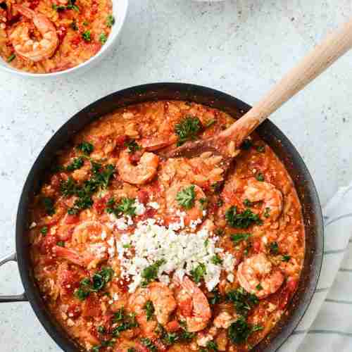 Poêle avec pâtes orzo cuites dans une sauce tomate et poivrons rôtis, avec crevettes et feta émietté