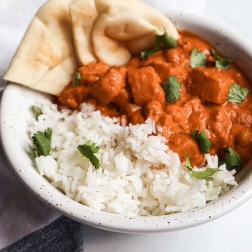 Bol de riz et de pois chiches et de courge dans une sauce tikka masala d'apparence orangée et crémeuse. On voit des morceaux de pain naan. Le tout est garni de coriandre fraîche ciselée.