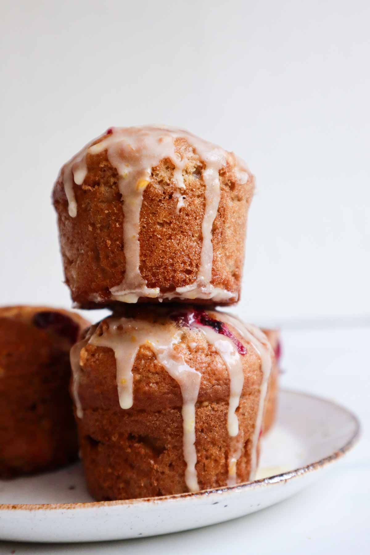 Muffins canneberges orange moelleux empilés sur une assiette, nappés d’un glaçage à l’orange.
