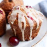 Muffin canneberges orange vu de près, avec glaçage coulant et morceaux de canneberges fraîches visibles.