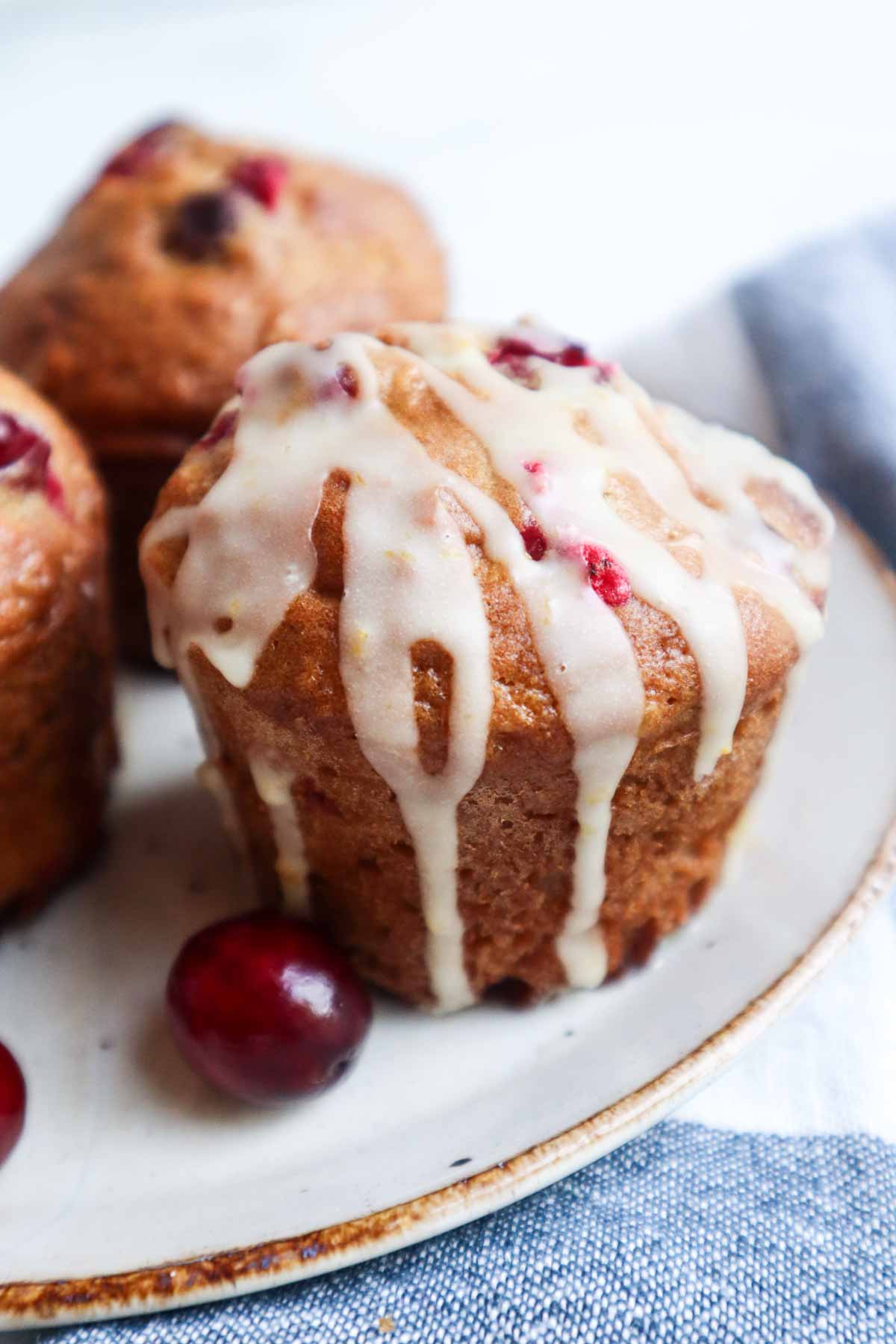 Muffin canneberges orange vu de près, avec glaçage coulant et morceaux de canneberges fraîches visibles.