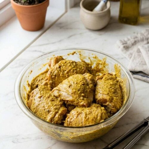 Dans un bol en verre, des hauts de cuisses de poulet enrobés de marinade shawarma, de texture épaisse à cause du yogourt, et de couleur jaune.