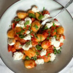 Gnocchis poêlés nappés de sauce tomate fraîche, garnis de bocconcini effiloché, de basilic frais et de pesto, servis dans un bol en grès.